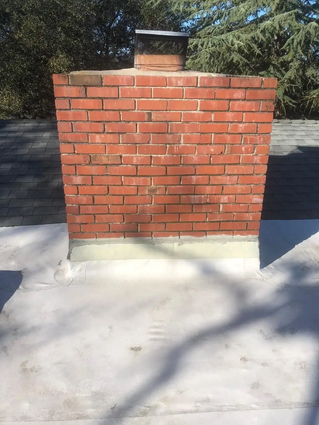 A red brick chimney on a flat roof, with metal flashing along its base.