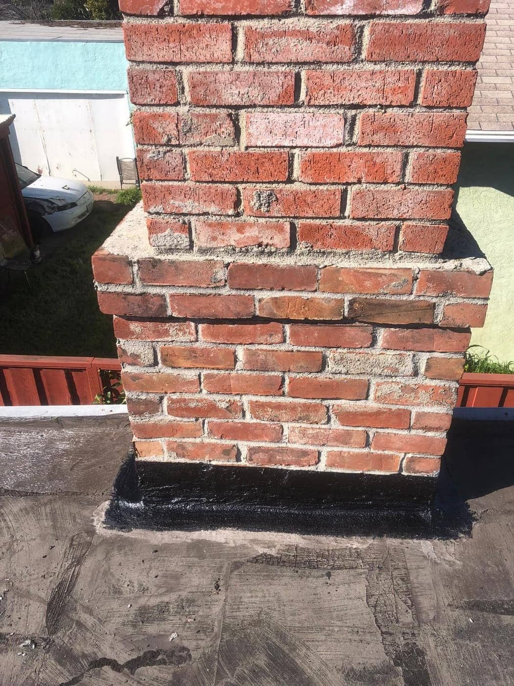 A red brick chimney on a flat roof, with black sealant around its base.