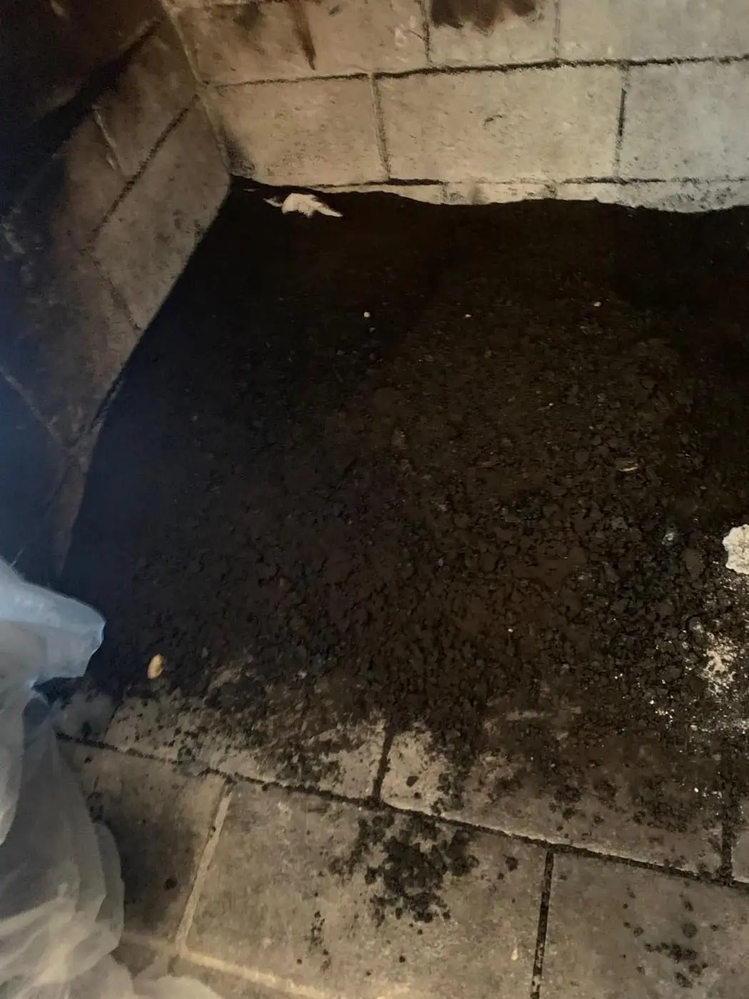 Soot and fallen debris on the floor of a fireplace, with plastic sheeting at the opening.