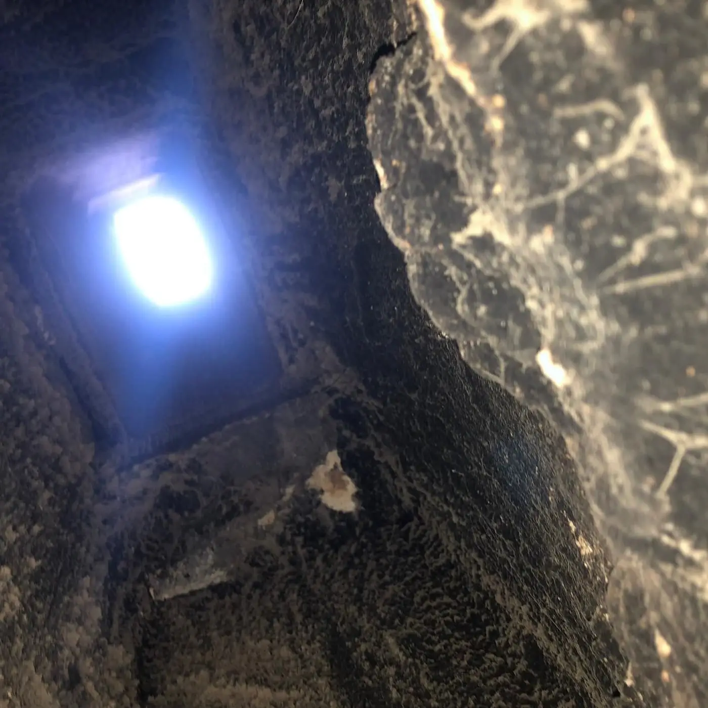 Vista hacia arriba de un conducto con una capa gruesa de residuo negro en las paredes, hacia una abertura iluminada arriba.